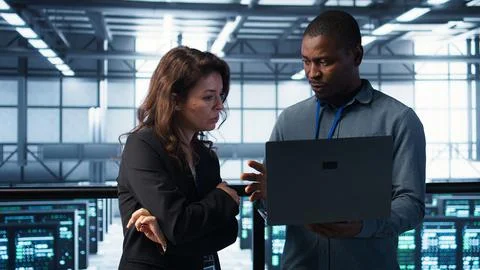 Developers in data center workspace coding on laptop, analyzing metrics 写真素材