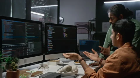 Developers Discussing Code on Computer Monitors in Office Stockbeeldmateriaal 348369876