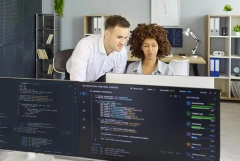 Developers pair programming and reviewing code on monitors in modern office Stock Photos