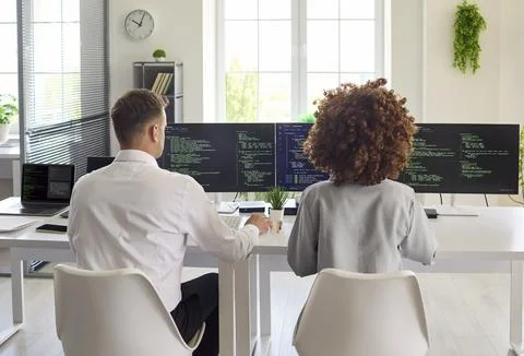 Developers pair programming at multi monitor workstation in modern bright office Stock Photos