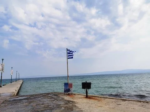 The developing flag of Greece on the background of the Mediterranean Sea. Stock Photos