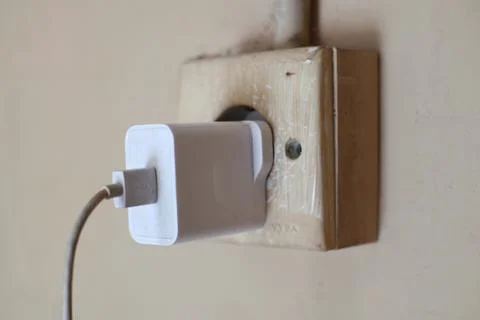 Device charger plugged into an aged wall socket, showing connectivity and p.. Stock Photos