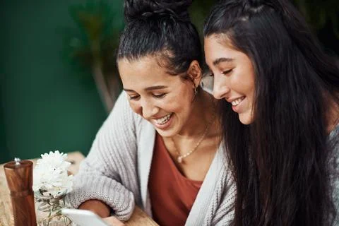The device made for sharing. young sisters using a smartphone together at a cafe Stock Photos