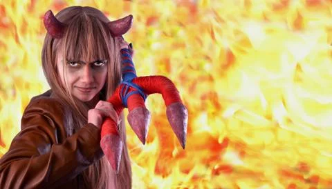 Devil girl with a trident in hands on a background of bright fire Stock Photos