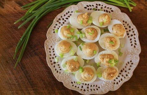 Deviled eggs with cod livers with leek on white plate. Rustic wooden table Stock Photos