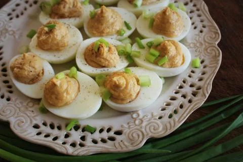 Deviled eggs with cod livers with leek on white plate. Rustic wooden table. T Stock Photos