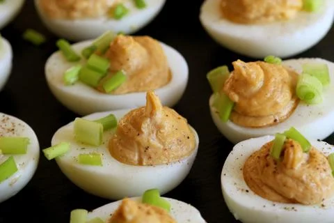 Deviled eggs with cod livers with leek on on black background Stock Photos