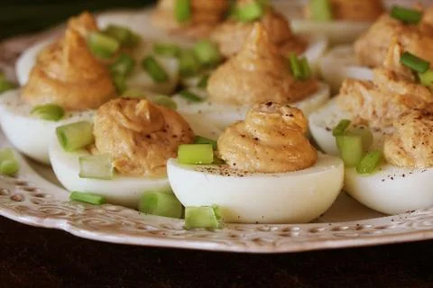 Deviled eggs with cod livers with leek on white plate. Rustic wooden table Stock Photos