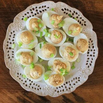 Deviled eggs with cod livers with leek on white plate. Rustic wooden table Stock Photos