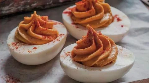 Deviled eggs topped with crispy bacon strips on a textured surface Stock Photos