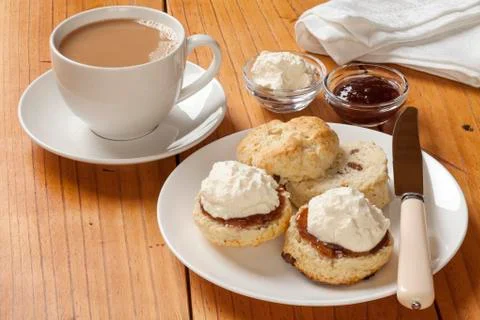 Devon cream tea, scones, jam, cream and a cup of tea, on an old pine table. Stock Photos