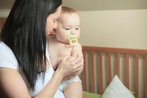 Devoted mother laying son down into crib for nap in bedroom 스톡 사진