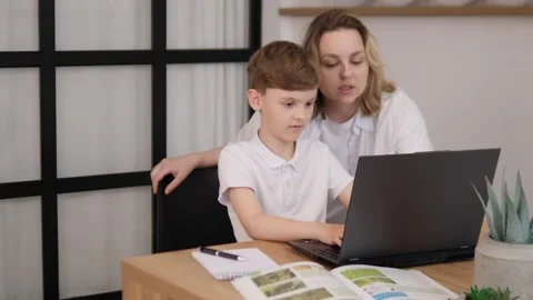 A devoted mother supports her childs online learning at home, aiding their Stock Footage 312220366