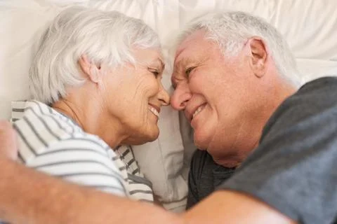 Devoted senior couple smiling warmly at each other in bed Stock Photos