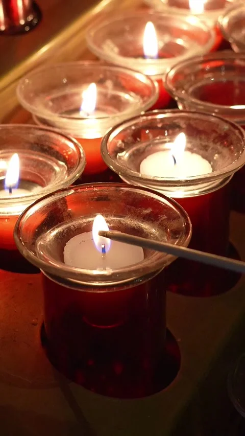 Devotee gently lighting votive candle inside church sanctuary 库存影片 311462468