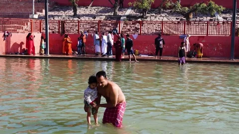Devotee Helping Young Child Take Holy Dip in Sacred Waters During Pilgrimage Stock Footage 340814445