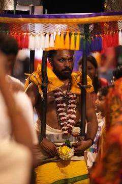 Devotee pauses during procession while attendants manage ritual bindings and Stock Photos