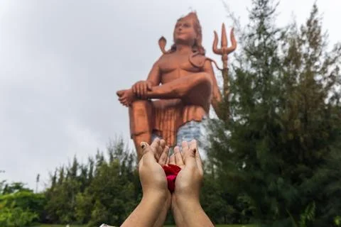 Devotee praying hand with flowers and blurred hindu god lord shiva statue a.. Stock Photos