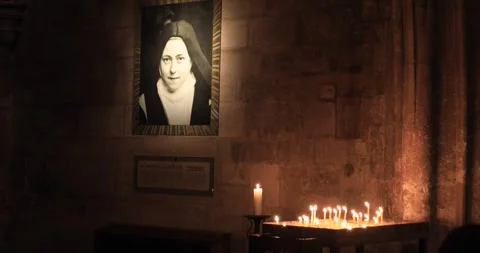Devotional corner with Therese of Lisieux saint portrait candles dim cathedral Stock Footage 321031212