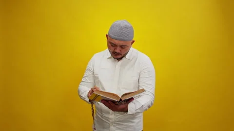 Devout Muslim Man Reading the Holy Quran on a Yellow Background Stock Footage 336994093