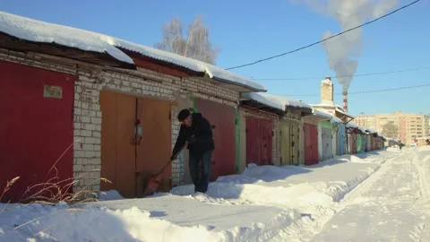 A dexterous man clears snow from the passage to the garage with a wooden shovel. Stock Footage 225416233