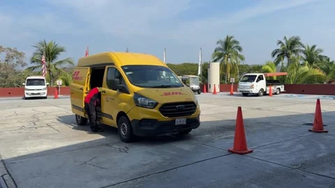 A DHL courier unloads a Ford transit van at a bright outdoor hub near palm trees Stock Footage 324891034
