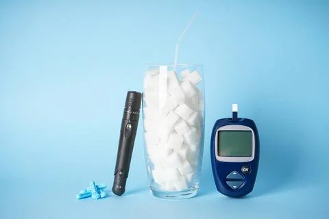 Diabetes concept. Digital glucometer, lanceolate pen, sugar in a glass on a b Foto stock