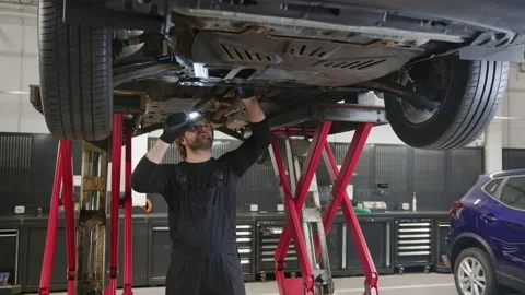 Diagnostics of the bottom of the car. An auto mechanic with a flashlight Stock Footage 240075999