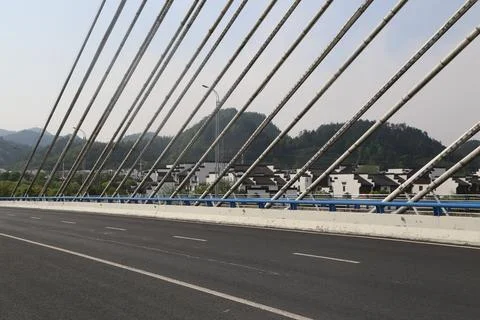 Diagonal bridge cables frame an empty road with white village houses and wo.. Stock Photos
