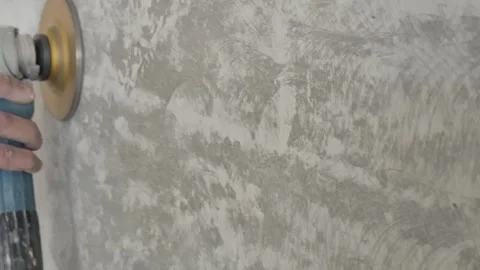 Diagonal close-up of electric hand grinder sanding concrete wall with dust Stock Footage 333326214