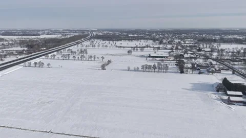 Diagonal highway through snowy fields, sparse trees, village buildings Stock Footage 327603484