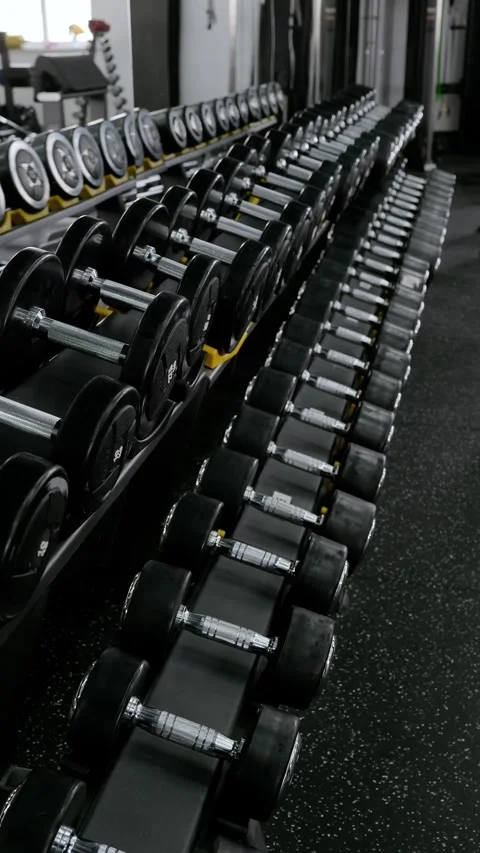 Diagonal rack of chrome handled rubber dumbbells in clean commercial gym Stock Footage 339347120