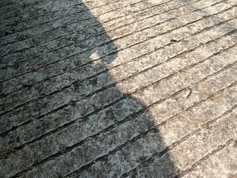 Diagonal shadow across rough gray stone pavement, sunlit textured surface b.. Stock Photos