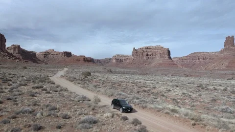 Diagonal tracking shot of black suv driving rugged dirt road through desert Stock Footage 124880994