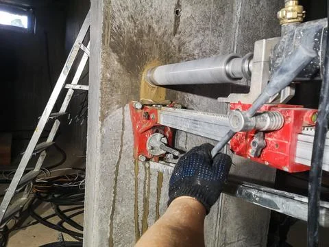 A diamond drill on a machine fixed to the wall drills a hole in concrete for an Stock Photos