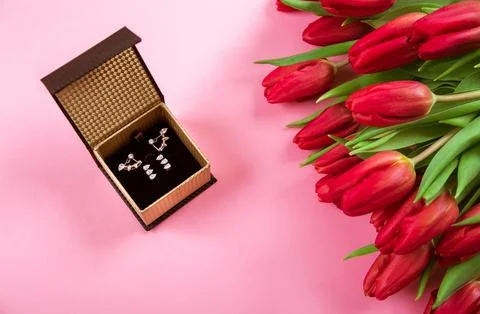 Diamond ring in box lais on a big bouquet of red tulips on pink background Stock Photos