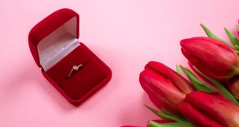 Diamond ring in box lais on a big bouquet of red tulips on pink background... Stock Photos