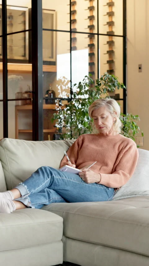 Diary, relax and writing with old woman on sofa in home living room for Stock Footage 337498416