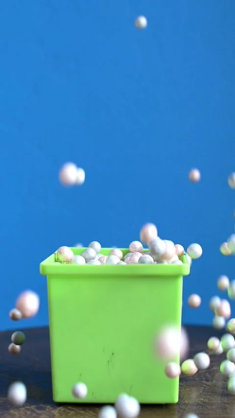 A dice  is falling into a green plastic box full of decorative Styrofoam balls. Stock Footage 327593552