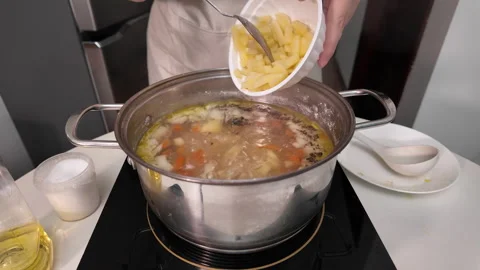 Diced potatoes are added to the boiling broth in a saucepan on an induction hob Stock Footage 319337159