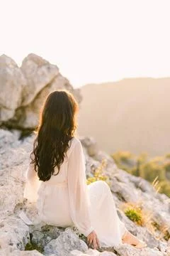 Die Braut sitzt auf einem Felsen in der Sonne und blickt auf die Berge. Rü.. Stock Photos