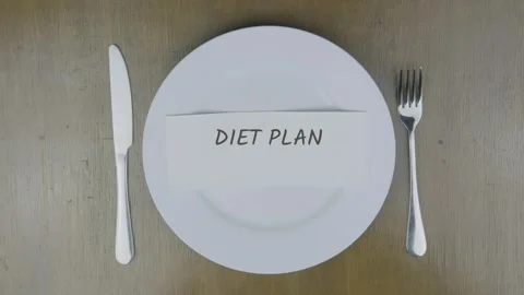 Diet plan word written on paper and hand putting it on white plate on table Stock Footage 313970197