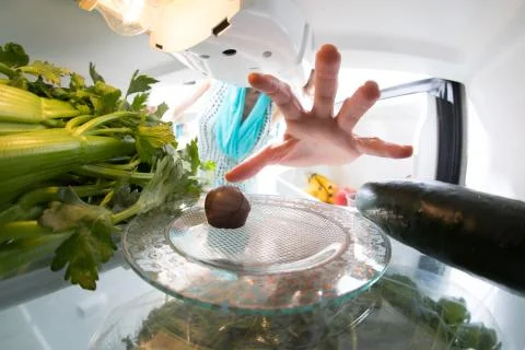 Diet struggle: A hand grabbing a tiny candy from the open refrigerator full of 스톡 사진
