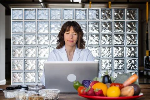 Dietitian working on laptop at table with assorted nutrient products Stock Photos