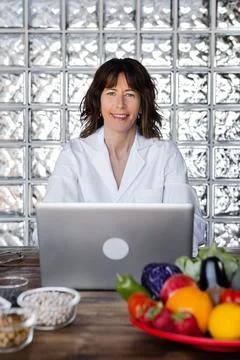 Dietitian working on laptop at table with assorted nutrient products Stock Photos