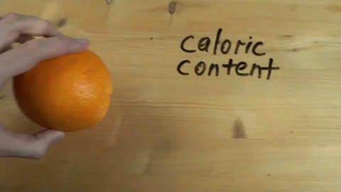 Dietologist hand writes down caloric content of orange on wooden surface Stock Footage 82905463