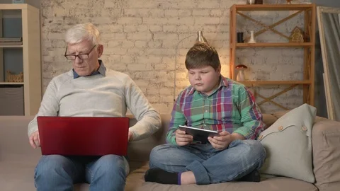 The difference of generations. Elderly man with glasses sitting on sofa working Stock Footage 85809227