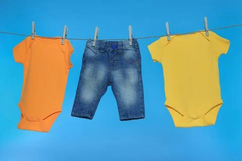 Different baby clothes drying on laundry line against light blue background Stock Photos