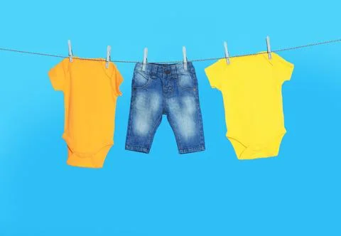 Different baby clothes drying on laundry line against light blue background Stock Photos