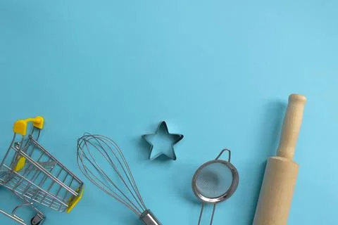 Different baking tools with shopping grocery cart on blue background, top view Stock Photos
